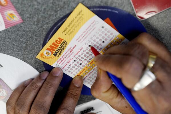 FILE - A customer fills out a Mega Millions lottery ticket at a convenience store in Northbrook, Ill., on Jan. 6, 2021. The holiday shopping season, for Mega Millions lottery ticket buyers, at least, is ramping up as officials say the estimated jackpot for the drawing the night of Tuesday, Dec. 27, 2022, has surpassed half a billion dollars. (AP Photo/Nam Y. Huh, File)