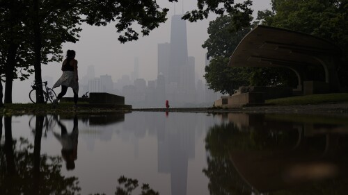 A person walks along the shore of Lake Michigan as the downtown skyline is blanketed in haze from Canadian wildfires Tuesday, June 27, 2023, in Chicago. (AP Photo/Kiichiro Sato)