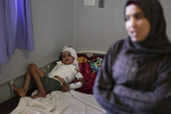Iman Abu Shabab, 30, stands next to her 7-year-old son, Hamza, who lies in bed with third-degree burns caused when, frightened by an Israeli airstrike, he spilled a hot plate of rice and lentils on himself in the family's tent in southern Gaza last month, at Nasser hospital in Khan Younis, Gaza Strip, Sunday, May 4, 2025.(AP Photo/Abdel Kareem Hana)