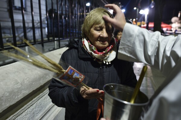 A priest blesses a pilgrim outside San Cayetano church in Buenos Aires, Argentina, before sunrise Wednesday, Aug. 7, 2024. Known as the patron saint of the unemployed, Catholics visit the church on the Italian Saint's feast day to pray for prosperity and work. (AP Photo/Gustavo Garello)
