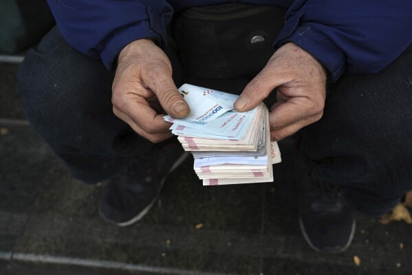 FILE - A street money exchanger poses for a photo without showing his face as he counts Iranian banknotes at a commercial district in downtown Tehran, Iran, Friday, Dec. 23, 2022. Iran’s currency fell to a record low on Sunday, plunging to 613,500 to the dollar, as its people celebrated the Persian New Year. (AP Photo/Vahid Salemi, File)
