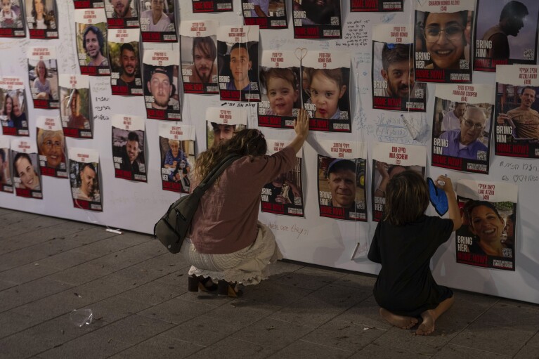 FILE - A woman touches photos of Israelis missing and held captive in Gaza, displayed on a wall in Tel Aviv on Oct. 21, 2023. (AP Photo/Petros Giannakouris, File)