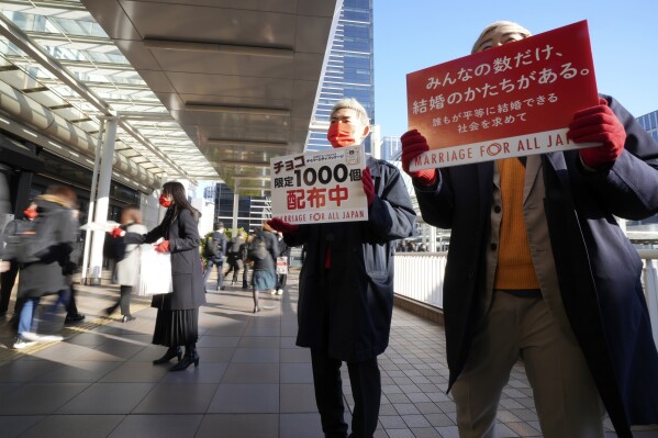 LGBTQ activists distribute chocolates to morning commuters at Shinagawa Station, marking the fifth anniversary of the day a group of plaintiffs launched their legal battle to achieve the marriage equality, to bolster the momentum toward pushing the government to provide the protection Wednesday, Feb. 14, 2024, in Tokyo. Banners read as "Everyone has their own way of getting married", left, and "We are distributing limited edition chocolates, to 1000 pieces." (AP Photo/Eugene Hoshiko)
