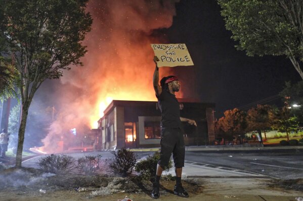 A person holds a sign as a Wendy's restaurant burns Saturday, June 13, 2020, in Atlanta after demonstrators set it on fire. Demonstrators were protesting the death of Rayshard Brooks, a black man who was shot and killed by Atlanta police Friday evening following a struggle in the Wendy's drive-thru line. (Ben GrayAtlanta Journal-Constitution via AP)