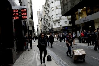 
              FILE - In this Aug. 30, 2018 file photo, people walk past an exchange house in Buenos Aires, Argentina. Argentina had hoped to show off its newly market-friendly economy to the world when the G-20 group of the world’s top economies begins its first South American summit in late November, but instead it’s looking for help to avoid an all-out crisis. (AP Photo/Natacha Pisarenko, File)
            