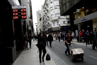 FILE - In this Aug. 30, 2018 file photo, people walk past an exchange house in Buenos Aires, Argentina. Argentina had hoped to show off its newly market-friendly economy to the world when the G-20 group of the world’s top economies begins its first South American summit in late November, but instead it’s looking for help to avoid an all-out crisis. (AP Photo/Natacha Pisarenko, File)