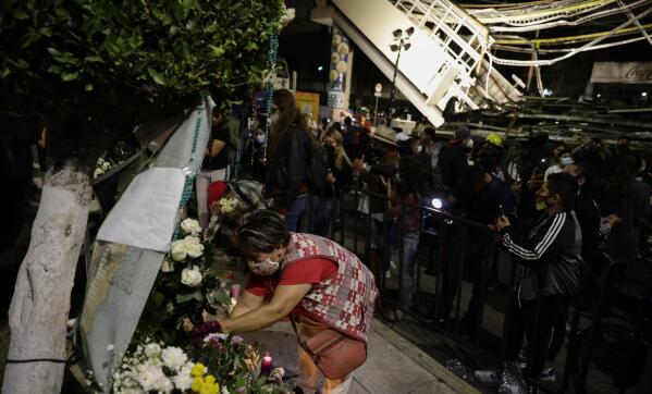 A woman places flowers at a makeshift altar during a protest demanding justice for the people who died in Monday's subway collapse, at the site of the wreckage in Mexico City's south side, Friday, May 7, 2021. An elevated section of Line 12 collapsed late Monday killing at least 25 people and injuring more than 70, city officials said. (AP Photo/Eduardo Verdugo)