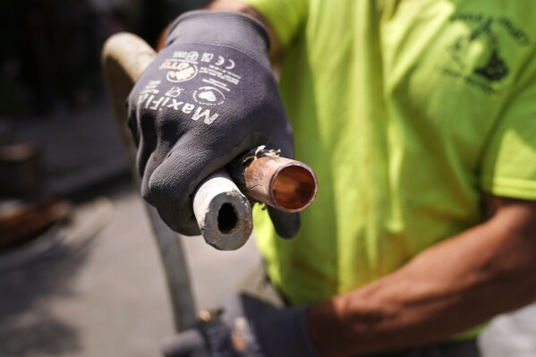 Richie Nero, of Boyle & Fogarty Construction, shows the the cross section of an original lead, residential water service line, at left, and the replacement copper line, at right, outside a home where service was getting upgraded, Thursday, June 29, 2023, in Providence, R.I. Health and environmental groups have been fighting for lead-free water to drink in Providence for at least a decade. (AP Photo/Charles Krupa)