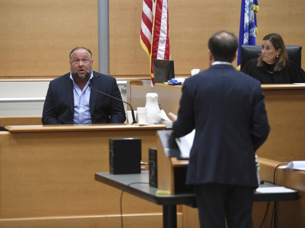 FILE - Infowars founder Alex Jones, left, is questioned by plaintiff's attorney Chris Mattei beside Judge Barbara Bellis, right, during testimony at the Sandy Hook defamation damages trial at Connecticut Superior Court in Waterbury, Conn. Thursday, Sept. 22, 2022. A $1.4 billion judgment was imposed against Jones for repeatedly calling the 2012 Newtown school shooting a hoax. (Tyler Sizemore/Hearst Connecticut Media via AP, Pool, File)