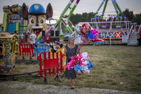 A balloon vendor walks at a fair in Hagioaica, Romania, Thursday, Sept. 14, 2023. For many families in poorer areas of the country, Romania's autumn fairs, like the Titu Fair, are one of the very few still affordable entertainment events of the year. (AP Photo/Vadim Ghirda)