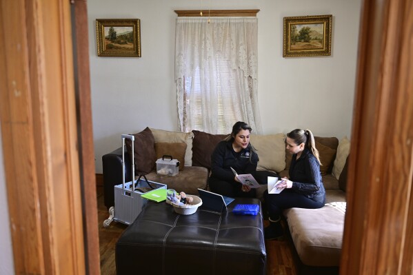 Instructor Mayra Ocampo, left, prepares materials before starting home visit instruction for Isabel Valencia in her living room in Pueblo, Colo., Wednesday, Feb. 28, 2024. Home visit programs have provided a lifeline for families, especially those for whom access to qualify early education is scarce or out of reach financially. The programs, which are set to expand with new federal support, are proven to help prepare children for school but have reached relatively few families. (AP Photo/Eric Lars Bakke)