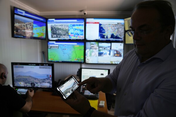 Grigoris Konstantellos, a commercial airline pilot and mayor of the southern Athens seaside suburbs of Vari, Voula and Vouliagmeni, shows on his cellphone the application of a drone warning system, at the control room in Voula, Athens, Greece, Thursday, Aug. 17, 2023. Greece is plagued by hundreds of wildfires each summer. To protect their area from potentially deadly blazes, a group of residents from a suburb in northern Athens have joined forces to hire a company using long-range drones equipped with thermal imaging cameras and a sophisticated early warning system to catch fires before they can spread. (AP Photo/Thanassis Stavrakis)