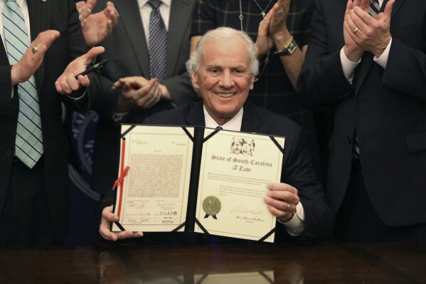 South Carolina Gov. Henry McMaster holds up a ceremonial copy of a bill allowing anyone who can legally own a gun to openly carry the weapon in the state at an event on Tuesday, March 19, 2024, in Columbia, S.C. McMaster signed the bill into law March 7. (AP Photo/Jeffrey Collins)