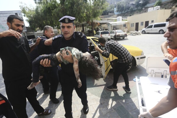FILE - A Hamas police officer carries a wounded girl into a hospital in Beit Lahiya, Gaza Strip, Sunday, Oct. 8, 2023. (AP Photo/Mahmoud Essa, File)