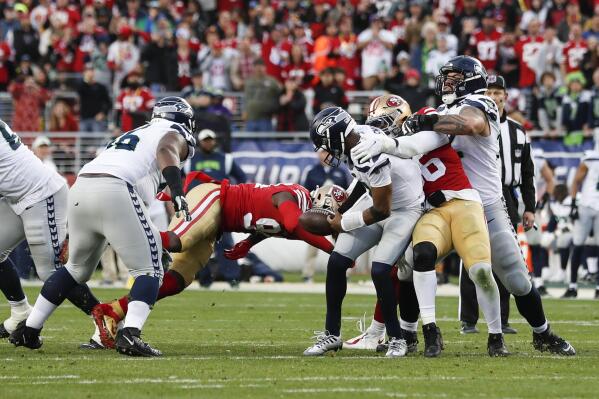 Seattle Seahawks quarterback Geno Smith, center right, fumbles the ball while sacked by San Francisco 49ers defensive end Charles Omenihu, center left, during the second half of an NFL wild card playoff football game in Santa Clara, Calif., Saturday, Jan. 14, 2023. The 49ers recovered the ball. (AP Photo/Jed Jacobsohn)
