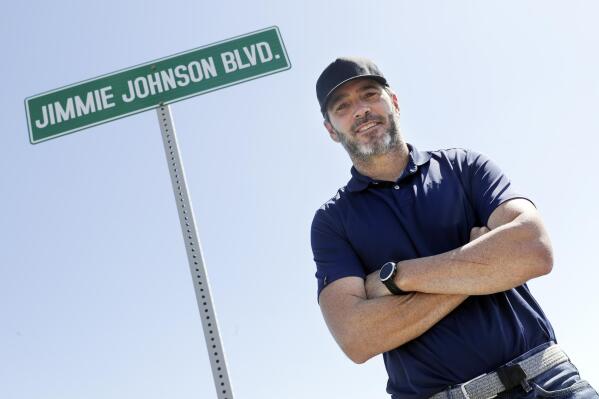 FILE - Driver Jimmie Johnson poses in front of a street sign after the street was named for him outside Kentucky Speedway before a NASCAR Cup Series auto race Sunday, July 12, 2020, in Sparta, Ky.  The Seven-time NASCAR champion is retiring from full-time racing and will turn his focus toward spending time with family. He figures his future schedule will include no more than 10 bucket list events and has his sights set on the 24 Hours of Le Mans. (AP Photo/Mark Humphrey, File)
