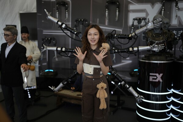 A woman poses in front of a six arm robot at the annual World Robot Conference at the Beijing Etrong International Exhibition and Convention Center in Beijing, Wednesday, Aug. 16, 2023. (AP Photo/Ng Han Guan)