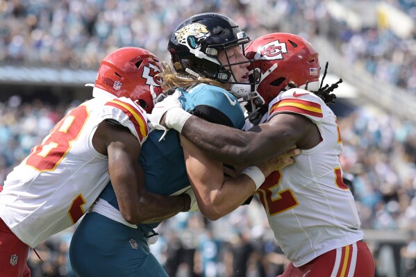 Jacksonville Jaguars quarterback Trevor Lawrence, center, is hit by Kansas City Chiefs cornerback L'Jarius Sneed, left, and Kansas City Chiefs linebacker Nick Bolton, right, during the second half of an NFL football game, Sunday, Sept. 17, 2023, in Jacksonville, Fla. (AP Photo/Phelan M. Ebenhack)