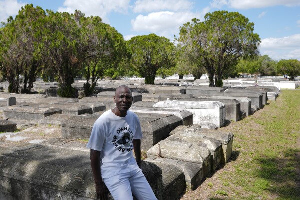 Jessie Wooden, owner of the Lincoln Memorial Park Cemetery, sits on a crypt, Monday, Feb. 26, 2024, in the Brownsville neighborhood of Miami. Wooden bought the cemetery after finding out that his mother, who died when he was an infant, was buried there. “All my life I didn’t know her. All I knew that mom was gone,” he says. “For me to be able to come where she’s resting at and be able to just to say a little prayer and talk to her, oh, that means so much to me.” (AP Photo/Marta Lavandier)