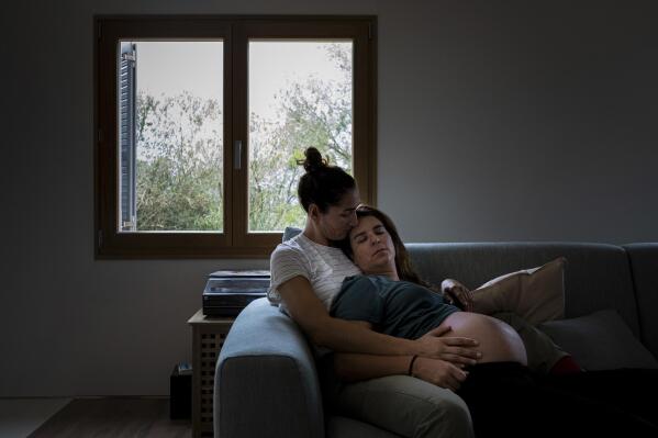 Polish Olympic athlete Jolanta Ogar-Hill, left, and her Spanish-British wife, the filmmaker Chuchie Hill sit on a sofa in their home in Palma de Mallorca, Spain, Wednesday, Nov. 10, 2021. When the Polish Olympic athlete Jolanta Ogar-Hill and her wife decided to have a baby, it was obvious to them both that Poland would not be the place to bring up their child. In recent years, right-wing ruling politicians and church leaders in the traditionally Roman Catholic nation have increased hostile rhetoric toward LGBT people, particularly as a way to mobilize conservative voters ahead of elections. (AP Photo/Francisco Ubilla)