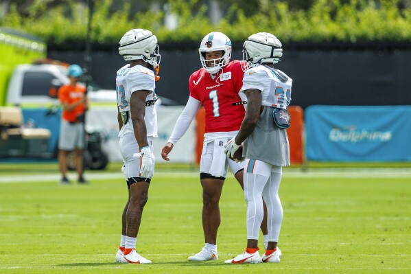 Miami Dolphins quarterback Tua Tagovailoa (1) talks with Dolphins running backs Raheem Mostert (31) and Jeff Wilson Jr. (23) during NFL football training camp at Baptist Health Training Complex in Hard Rock Stadium on Thursday, Aug. 3, 2023 in Miami Gardens, Fla. (David Santiago/Miami Herald via AP)