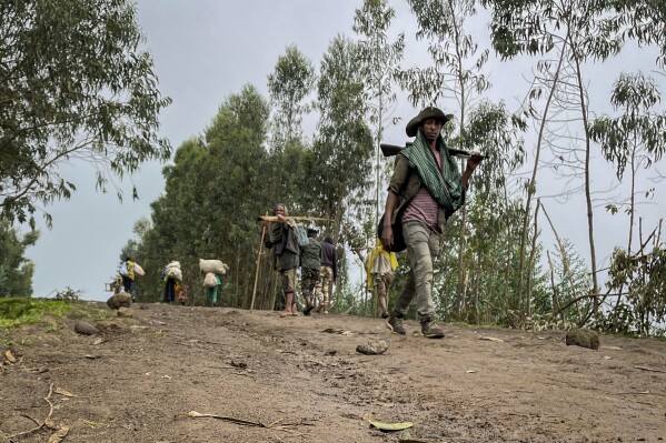 FILE — An unidentified armed militia fighter walks down a path as villagers flee with their belongings in the other direction, near the village of Chenna Teklehaymanot, in the Amhara region of northern Ethiopia Thursday, Sept. 9, 2021. Ethiopia's government and residents say the military has recaptured several areas in the embattled Amhara region from local militia fighters, while details of dozens of civilians killed have begun to emerge from the region amid an internet shutdown. The military has reclaimed control of six towns including the regional capital of Bahir Dar and the region's second-largest town, Gondar, according to a government statement on Wednesday, Aug. 9, 2023. It said curfew has been imposed in those areas and flights there are set to resume. (AP Photo, File)