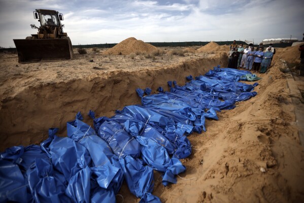 Palestinians pray over bodies of people killed in the Israeli bombardment who were brought from the Shifa hospital before burying them in a mass grave in the town of Khan Younis, southern Gaza Strip, Wednesday, Nov. 22, 2023. (AP Photo/Mohammed Dahman)