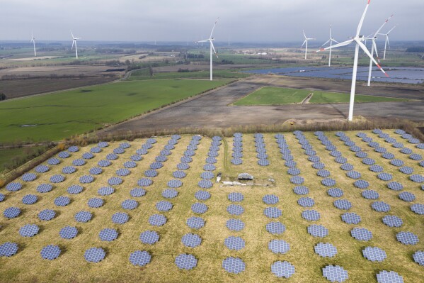 Solar panels stand on the edge of a wind farm in Sprakebuell, Germany, Thursday, March 14, 2024. Sprakebuell is something of a model village for the energy transition - with an above-average number of electric cars, a community wind farm and renewable heat from biogas. All houses in the village center have been connected to the local heating network and all old oil heating systems have been removed. Aerial photography with a drone. (AP Photo/Frank Molter) (AP Photo/Frank Molter)