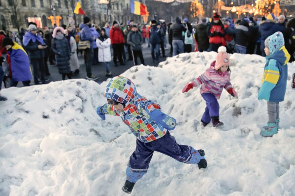 
              A child plays with snow, backdropped by adults wrapped in European Union and Romanian flags during a protest in Bucharest, Romania, Saturday, Dec. 22, 2018. More than 1,000 Romanians have demanded more democracy during an anti-government march to commemorate the victims of 1989 anti-communist revolt. (AP Photo/Vadim Ghirda)
            