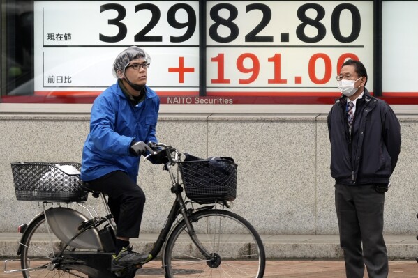 Persons wait for traffic signal to change in front of an electronic stock board showing Japan's Nikkei 225 index at a securities firm Tuesday, Dec. 12, 2023, in Tokyo. Asia markets opened higher following a positive close on Wall Street. Investors are eagerly awaiting a crucial U.S. inflation report later in the day, which will likely set the tone for the Federal Reserve’s final meeting of the year on Wednesday.(AP Photo/Eugene Hoshiko)