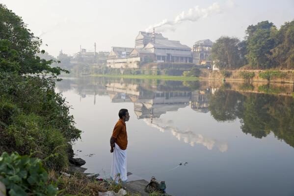 Adam Kutty stands on the bank of the Periyar River with smokestacks in the distance in Eloor, Kerala state, India, Friday, March 3, 2023. Many of the petrochemical nearby produce pesticides, rare earth elements, rubber processing chemicals, fertilizers, zinc-chrome products and leather treatments. (AP Photo)