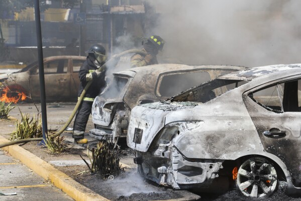 Firefighters douse water on cars at the state's Attorney General's Office set on fire by students from a rural teachers' college protesting the shooting of one of their colleagues during a confrontation with police the previous week in Chilpancingo, Mexico, Tuesday, March 12, 2024. (AP Photo/Alejandrino Gonzalez)