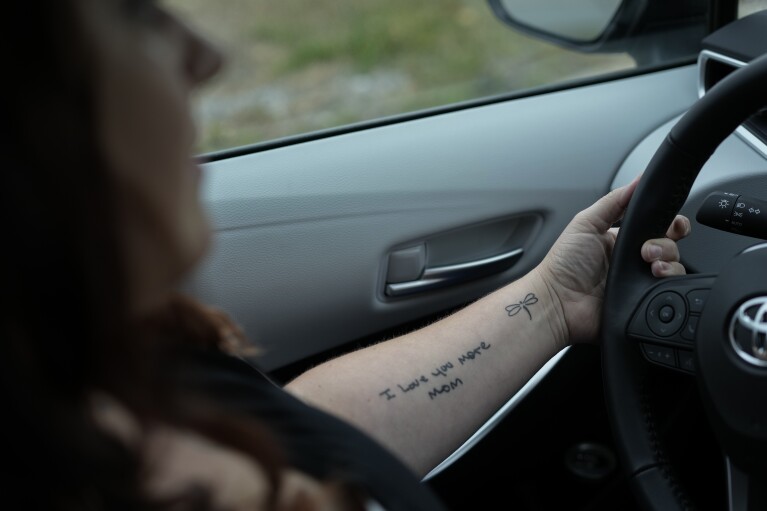 Jesse Johnson of the Family Resource Center drives to pick up a client and take them to the pharmacy in Findlay, Ohio, Thursday, Oct. 12, 2023. The tattoo on her forearm reads "I love you more, Mom," is from a birthday card her mother gave her before she died. Johnson was newly in recovery when her mother died from COVID in 2021. (AP Photo/Carolyn Kaster)