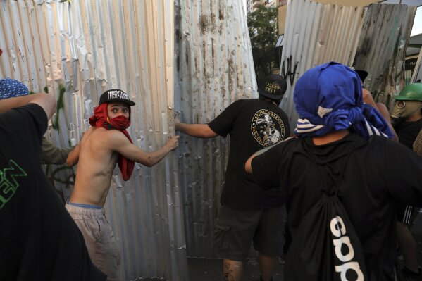 Protesters use metal sheets as shields during clashes with police during anti-government protests in Santiago, Chile, Thursday, Oct. 24, 2019. A new round of clashes and looting broke out Thursday as demonstrators returned to the streets, dissatisfied with economic concessions announced by the government in a bid to curb a week of deadly violence. (AP Photo/Rodrigo Abd)