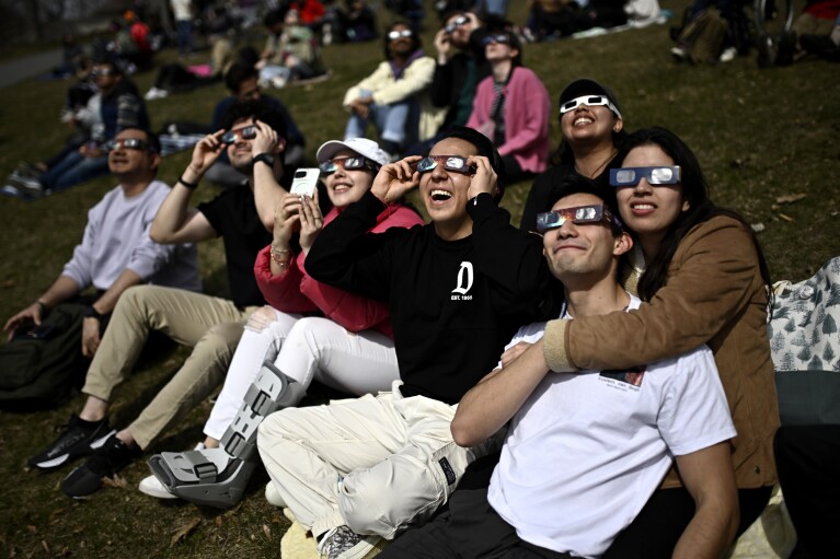 يرتدي الناس نظارات كسوف الشمس وهم يراقبون المرحلة الجزئية من كسوف الشمس الكلي، في كينغستون، أونتاريو، الاثنين 8 أبريل 2024. (جاستن تانغ / الصحافة الكندية عبر AP)