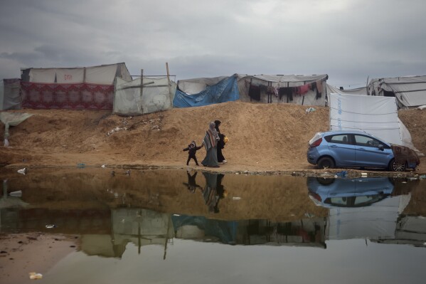 Palestinians displaced by the Israeli ground offensive on the Gaza Strip walk through a flooded makeshift tent camp in Rafah, Gaza Strip, Sunday, Feb. 18, 2024. (AP Photo/Mohammed Dahman)