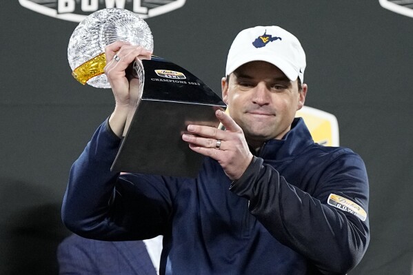 FILE - West Virginia head coach Neal Brown gets holds the trophy after their win against North Carolina in an NCAA college football game at the Duke's Mayo Bowl Wednesday, Dec. 27, 2023, in Charlotte, N.C. Brown has agreed to a $400,000 pay cut over the next three years while being rewarded with a one-year contract extension through 2027 following a nine-win season. (AP Photo/Chris Carlson, File)