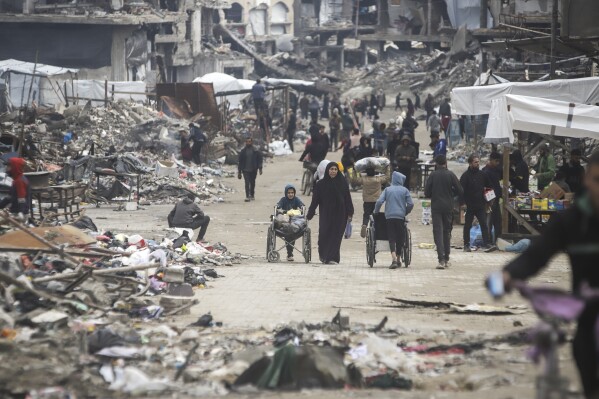 The pedestrians walk along a road bordered by few stands selling goods, in the middle of generalized destruction caused by the refugee camp in Gaza City, Friday, February 7, 2025. (AP photo / Jehad Alshrafi)