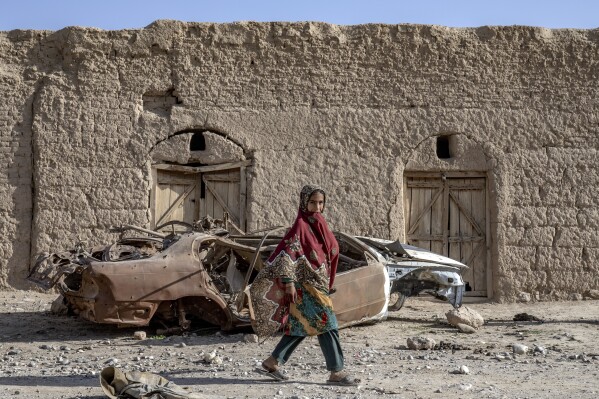 A girl walks past a destroyed car in a village in a remote region of Afghanistan, on Saturday, Feb. 25, 2023. (AP Photo/Ebrahim Noroozi)