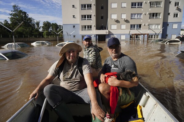 La gente rescata a Mia, una perra, de una zona inundada después de fuertes lluvias en Canoas, estado de Rio Grande do Sul, Brasil, el jueves 9 de mayo de 2024.  (Foto AP/Carlos Macedo)
