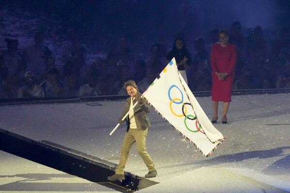 Tom Cruise holds the Olympic flag during the 2024 Summer Olympics closing ceremony at the Stade de France, Sunday, Aug. 11, 2024, in Saint-Denis, France. (AP Photo/Martin Meissner)