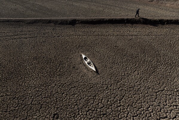 FILE - A man walks past an abandoned canoe at the Sau reservoir amid a drought in Vilanova de Sau, north of Barcelona, Spain, Jan. 26, 2024. (AP Photo/Emilio Morenatti File)