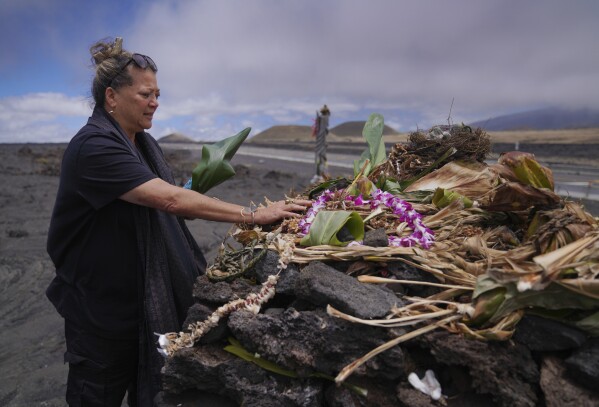 Kealoha Pisciotta, a cultural practitioner and longtime activist, lays offerings before praying at an "ahu," or ceremonial platform, part of the way up Mauna Kea in Hawaii, on Saturday, July 15, 2023. Along the slopes of this sacred mountain are ceremonial platforms, ancestral burial sites, and an alpine lake whose waters are believed to have healing properties. (AP Photo/Jessie Wardarski)