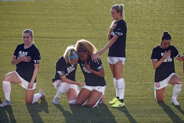 FILE - In this June 27, 2020, file phohto, Chicago Red Stars' Julie Ertz, second from left, holds Casey Short, center, while other players for the team kneel during the national anthem before an NWSL Challenge Cup soccer match against the Washington Spirit at Zions Bank Stadium in Herriman, Utah. The National Women's Soccer League revised its anthem policy after most players knelt during the anthem before season-opening games last weekend at the Challenge Cup. (AP Photo/Rick Bowmer, File)