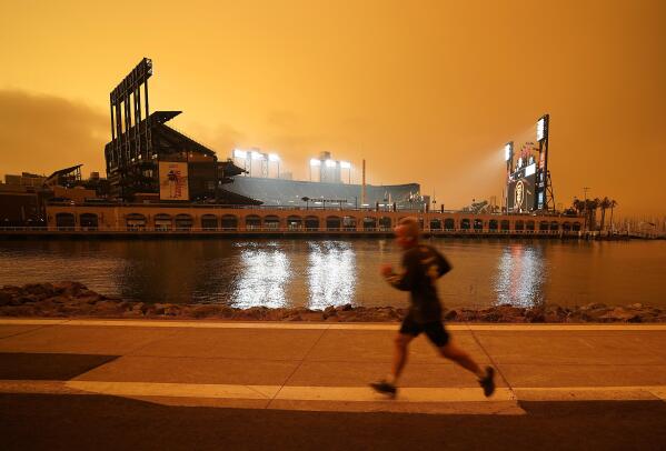 FILE - In this Wednesday, Sept. 9, 2020 file photo, a jogger runs along McCovey Cove outside Oracle Park in San Francisco, under darkened skies from wildfire smoke. Worsening climate change requires that the United States do much more to track and manage flows of migrants fleeing natural disasters. That's the finding of a multiagency study from the Biden administration. President Joe Biden ordered the assessment.   (AP Photo/Tony Avelar)