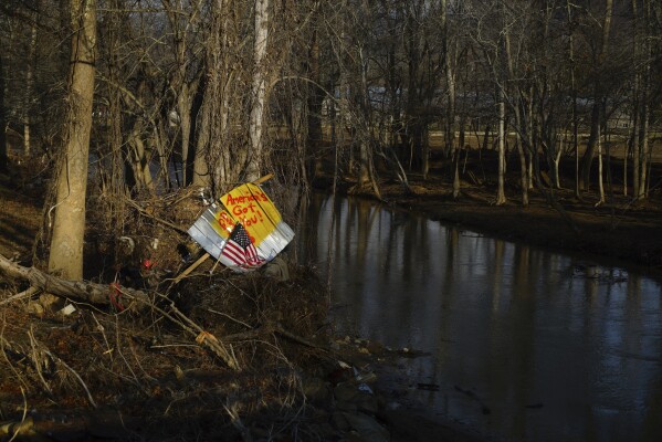 A piece of debris with an American flag and inspirational message stand along a riverbank in Swannanoa, N.C., on Friday, Feb. 7, 2025. More than four months after the remnants of Hurricane Helene devastated western North Carolina, many residents are frustrated with the federal response. (AP Photo/Allen G. Breed)