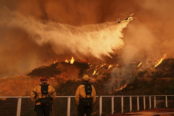 Firefighters watch a helicopter drop water on the Palisades Fire in Mandeville Canyon in Los Angeles, Jan. 11, 2025. (AP Photo/Jae C. Hong, File)