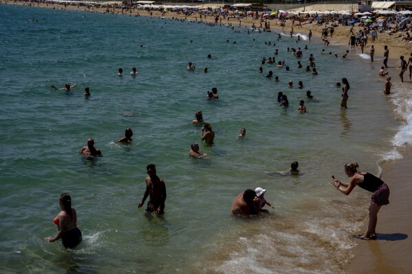 ARCHIVO - Personas refrescándose en una playa de Barcelona, ​​​​España, 9 de agosto de 2023. Los últimos cálculos de varias agencias científicas del viernes 12 de enero de 2024 indican que las temperaturas promedio globales para 2023 batieron los récords de calor actuales.  (Foto AP/Emilio Morenatti)