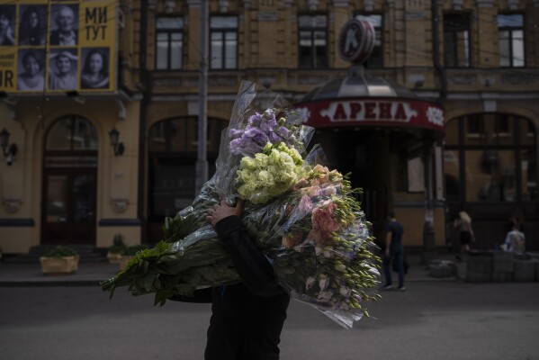 FILE - A vendor carries bundles of flowers in Kyiv, Ukraine, Monday, July 10, 2023. Life in the capital of a war-torn country seems normal on the surface. In the mornings, people rush to their work holding cups of coffee. Streets are filled with cars, and in the evenings restaurants are packed. But the details tell another story. (AP Photo/Jae C. Hong, File)