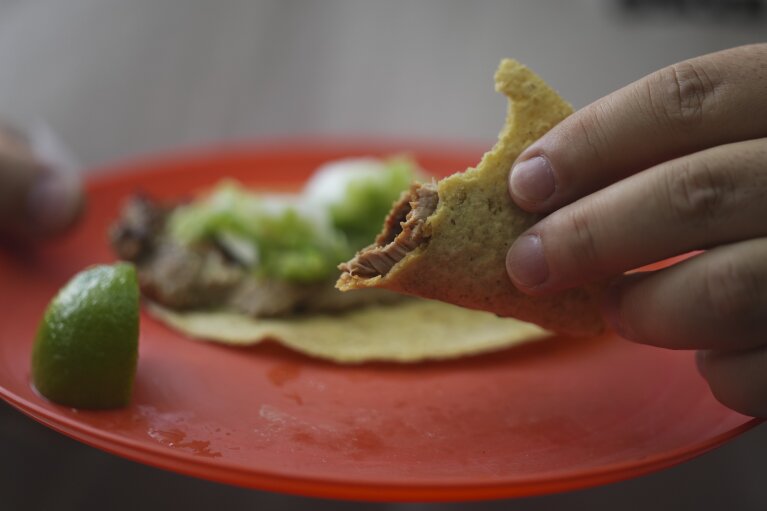 Een klant houdt een gedeeltelijk opgegeten taco vast bij tacokraam Tacos El Califa de León, in Mexico-Stad, woensdag 15 mei 2024. Tacos El Califa de León is het eerste tacokraam ooit dat een Michelinster heeft gekregen van de Franse voedselgids.  (AP-foto/Fernando Llano)